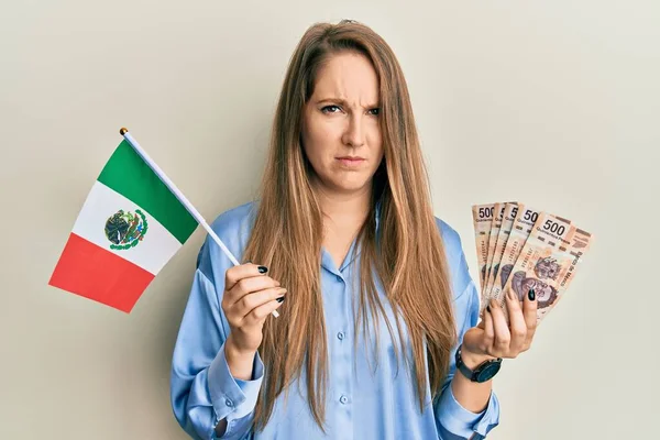 メキシコの国旗とメキシコのペソ紙幣を持つ若いブロンドの女性は懐疑的で緊張しており 問題のために動揺している 否定的な人 — ストック写真