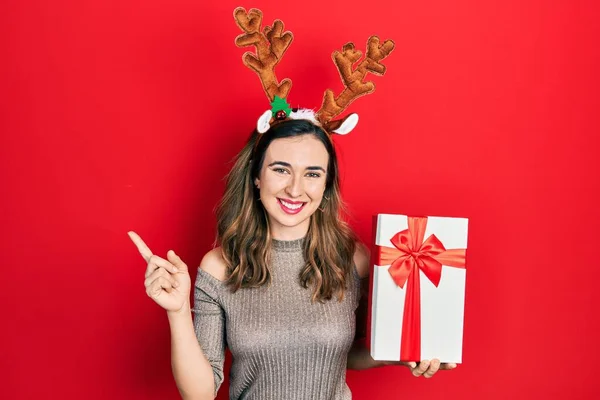 Νεαρό Ισπανόφωνο Κορίτσι Φορώντας Ελάφι Χριστουγεννιάτικο Καπέλο Κρατώντας Δώρο Χαμογελώντας — Φωτογραφία Αρχείου