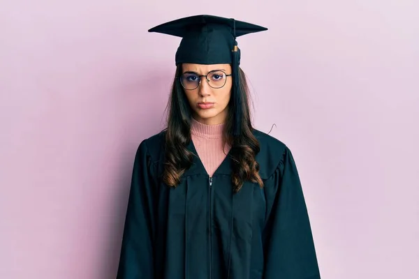 卒業キャップと式のローブを着た若いヒスパニック系の女性は懐疑的で緊張し 問題のために動揺を眉をひそめています 否定的な人 — ストック写真