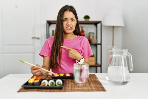 年轻的黑发女人用筷子吃寿司 用食指把焦虑和紧张放在一边 关切和惊讶的表情 — 图库照片