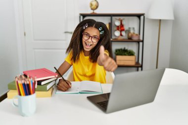 Young african american girl doing homework at home approving doing positive gesture with hand, thumbs up smiling and happy for success. winner gesture. 