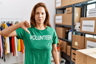 Orta yaşlı İspanyol kadın bağışlarda gönüllü tişört giyer kızgın suratlı, olumsuz işaretli baş parmakları aşağıda, reddedilme konsepti var. 