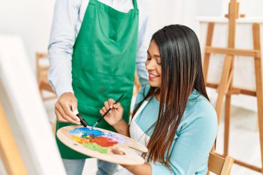 Resim stüdyosunda gülümseyen genç Latin ressam çift.