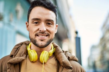 Şehirde kulaklık takarak mutlu gülümseyen genç İspanyol adam..