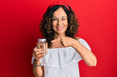 Orta yaşlı İspanyol kadın elinde cevizli kavanoz tutarken mutlu mesut elini ve parmağını gösteriyor. 