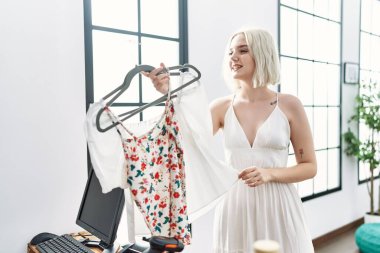 Giysi dükkanında kendine güvenen beyaz bir kadın gülümsüyor.