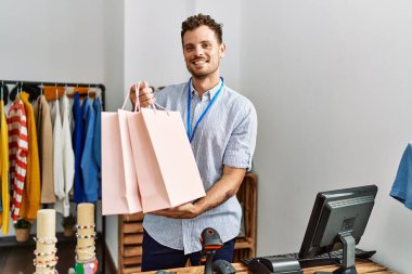 Genç İspanyol esnaf mağazada alışveriş torbalarını tutarken mutlu gülümsüyor..