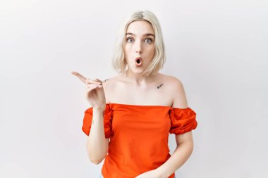 Kafkasyalı genç bir kadın izole edilmiş arka planda durup parmağını yana doğru kaldırarak şaşırdı, ağzı açık hayret içinde kaldı.. 