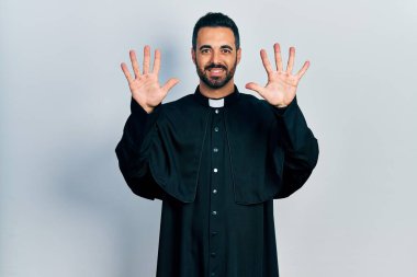 Sakallı, Katolik rahip cüppeli yakışıklı bir adam on numaralı parmaklarıyla kendini beğenmiş ve mutlu gülümserken kendini gösteriyor.. 