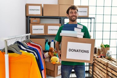 Hayır kurumunda bağış kutusu ve kitapları elinde tutmaktan mutlu gülümseyen genç İspanyol gönüllü adam..