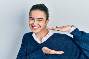 Kafkasyalı genç bir kız, günlük kıyafetler giyiyor. Elleriyle işaret ediyor. Büyük ve büyük beden işareti, ölçü işareti. Kameraya bakıp gülümsüyor. ölçüm kavramı. 