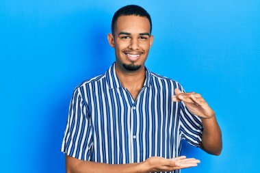 Genç Afrikalı Amerikalı sıradan kıyafetler giyen, elleri büyük ve büyük boy işareti gösteren, ölçü sembolü olan bir adam. Kameraya bakıp gülümsüyor. ölçüm kavramı. 