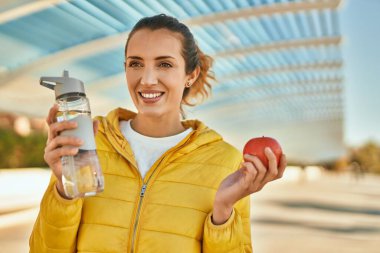 Genç İspanyol kız şehirde bir şişe su içip elma yiyor..