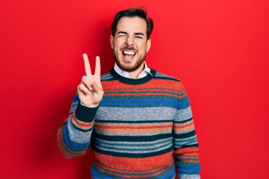 Sakallı, zarif yün süveter giyen, kameraya gülümseyen ve zafer işareti yapan yakışıklı beyaz adam. İki numara.. 