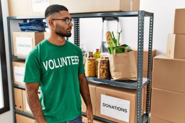 Genç Hintli gönüllü bağış kutusunu tutuyor. Yan tarafa bakıyor, rahat poz veriyor. Kendine güvenen bir gülümsemesi var.. 