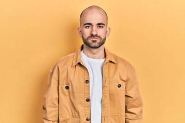 Yüzünde ciddi bir ifade olan günlük kıyafetler giyen genç kel bir adam. Basit ve doğal bir şekilde kameraya bakıyorsun.. 