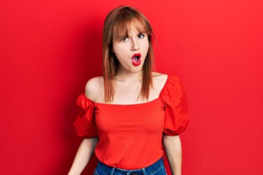 Kırmızı tişörtlü, şaşkın bakışlı, kuşkucu ve alaycı bakışlı, ağzı açık bir şekilde şaşırmış genç bir kadın. 