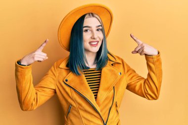 Sarı şapkalı ve deri ceketli genç modern kız iki eliyle başını gösteren gülümseme, harika bir fikir ya da düşünce, iyi bir hafıza 