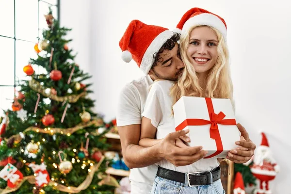 Young Couple Wearing Christmas Hat Hugging Holding Gift Home — Stock Photo, Image