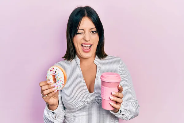 Young Hispanic Woman Eating Doughnut Drinking Coffee Winking Looking Camera — Stock Photo, Image