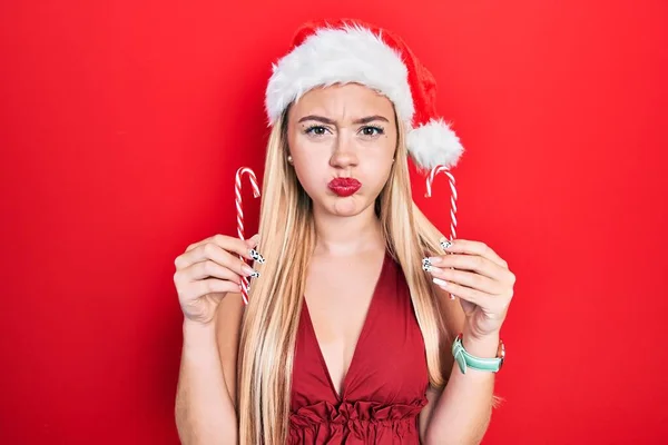 若いブロンドの女の子は 面白い顔でキャンディパフ頬を保持クリスマスの帽子を身に着けています 空気を吸い込み空気を吸い込み — ストック写真