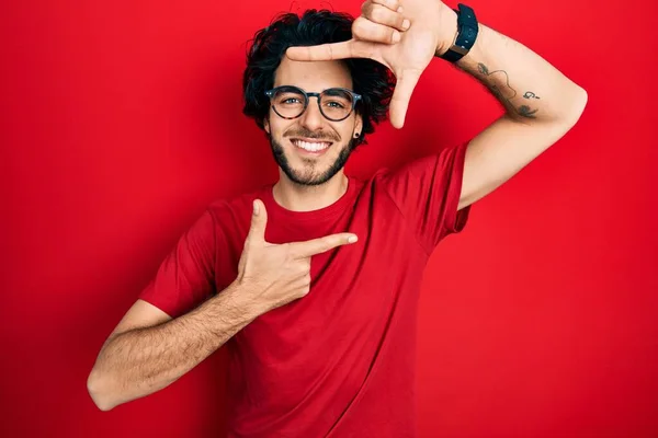 カジュアルなTシャツを着たハンサムなヒスパニック系の男性と 幸せな顔をした手と指でフレームを作る笑顔メガネ 創造性と写真の概念 — ストック写真