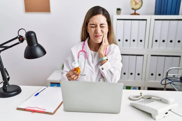 Młoda Latynoska Mundurze Lekarskim Trzymająca Tabletki Klinice Dotykająca Ust Bolesnym — Zdjęcie stockowe
