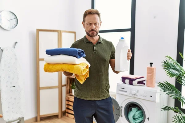 Medelålders Man Som Håller Ren Tvätt Och Tvättmedel Flaska Skeptisk — Stockfoto
