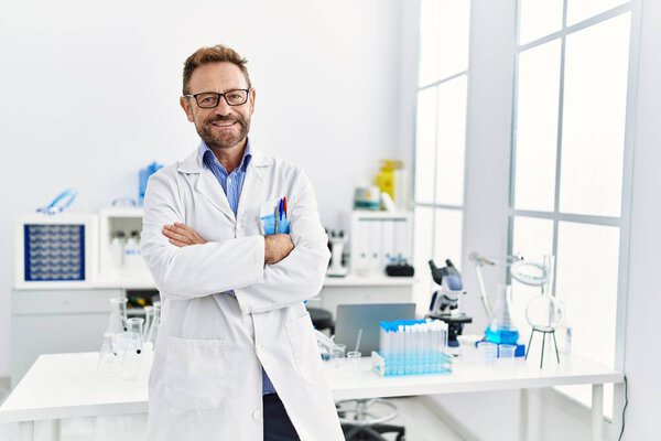 Middle age hispanic man wearing scientist uniform with arms crossed gesture at laboratory