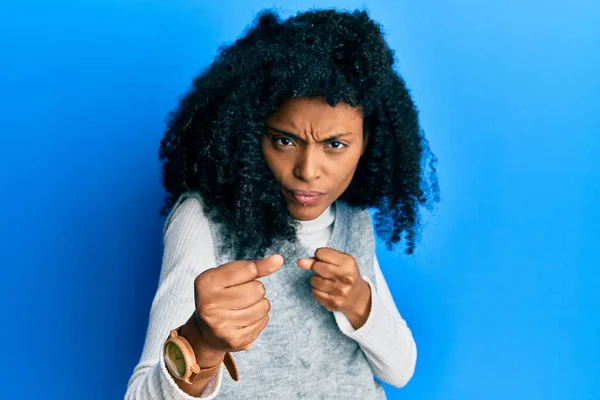 アフリカ系アメリカ人女性とアフロの髪を身に着けているカジュアル冬のセーターで戦う準備ができている拳の防衛ジェスチャー 怒りと動揺の顔 問題を恐れて — ストック写真