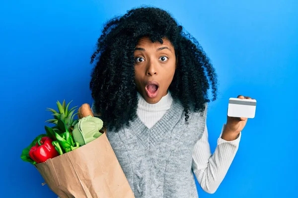 アフリカ系アメリカ人の女性が食料品やクレジットカードを持っているアフロの髪を恐れていると驚きと驚きの表情でショックを受けました 恐怖と興奮した顔 — ストック写真