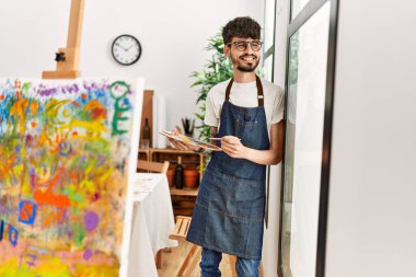Genç İspanyol ressam mutlu bir şekilde resim stüdyosunda duruyor..
