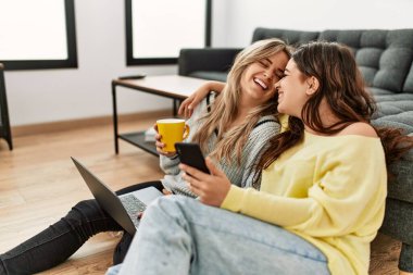 Laptop ve akıllı telefon kullanan genç bir çift evde kahve içiyor..