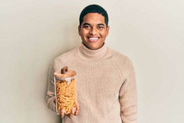 Genç, yakışıklı, elinde makarna dolu kavanoz tutan yakışıklı bir adam. Olumlu ve mutlu görünüyor. Kendine güvenen bir gülümsemeyle dişlerini gösteriyor. 