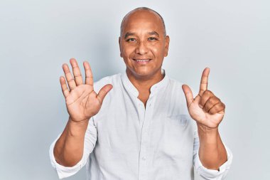 Orta yaşlı, gündelik kıyafetler giyen Latin bir adam 7 numarayı gösterip işaret ederken kendine güvenen ve mutlu bir şekilde gülümsüyor.. 