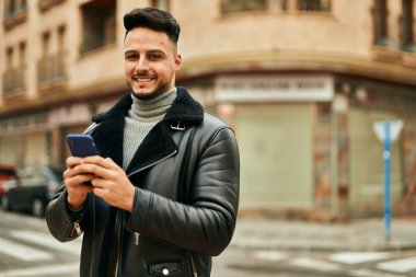 Genç Arap adam şehirde akıllı telefon kullanarak mutlu gülümsüyor..