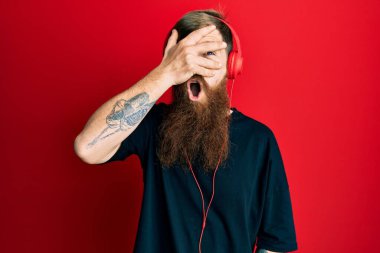 Kızıl saçlı, uzun sakallı, müzik dinleyen kulaklık takan, şok içinde yüzünü ve gözlerini kapayan, utangaç ifadesiyle parmaklarından bakan bir adam.. 