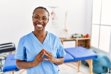 Saçları örgülü zenci bir kadın. Klinikte çalışıyor. Ellerini birleştirip gülümsüyor ve rahatlıyor. Başarı ve iyimserlik 