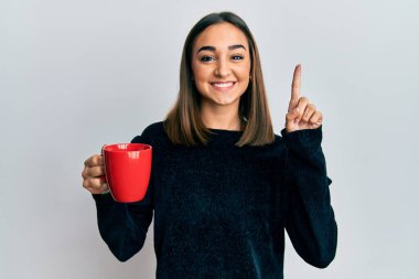 Kahvesini yudumlayan esmer bir genç kız bir fikirle gülümsüyor ya da bir soru işareti yapıyor. 