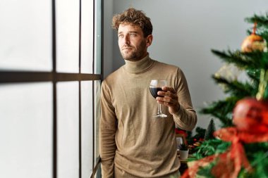 Genç İspanyol adam evde Noel ağacının yanında şarap içiyor.
