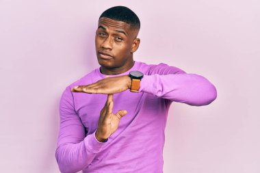 Genç siyah bir adam pembe kazak giyiyor. Elleriyle jest yapıyor, hayal kırıklığına uğramış ve ciddi bir yüz ifadesi takınıyor. 