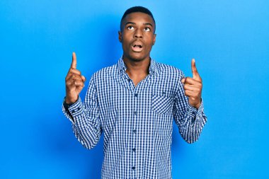 Gündelik giysiler giyen genç Afro-Amerikan adam şaşkın ve şaşırmış bir şekilde yukarı baktı ve parmaklarıyla işaret etti ve kollarını kaldırdı.. 