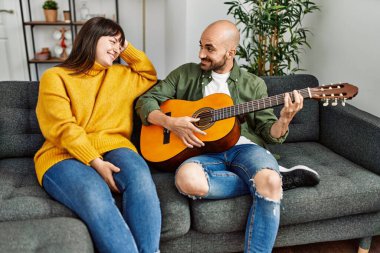 Genç İspanyol çift gülümseyerek evde kanepede oturmuş klasik gitar çalıyor..