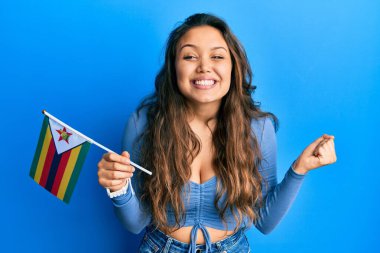 Genç İspanyol kız elinde zimbabwe bayrağı tutarken gururla bağırıyor, zaferi kutluyor ve kollarını kaldırdığı için heyecanlanıyor. 