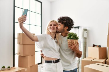 Genç ve güzel bir çift mutlu bir şekilde gülümsüyor. Yeni evlerinde akıllı telefonların yanında selfie çekiyorlar..