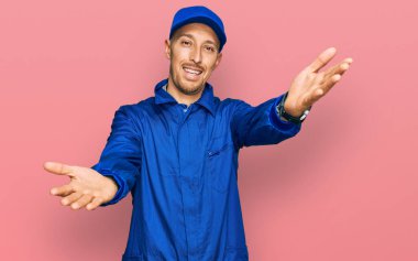 Sakallı, inşaatçı tulumu giymiş kel bir adam kameraya sarılıp gülümsüyor. Mutluluğu kucaklayan neşeli bir ifade.. 