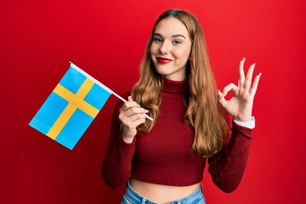 年轻的金发女子举着瑞典国旗 手拿着手签 微笑着表示友善的手势 是个很好的象征 — 图库照片