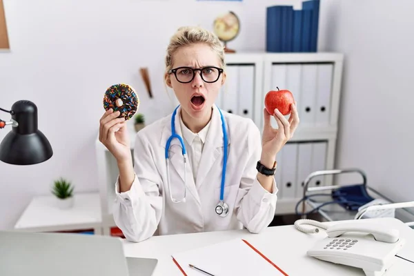 Joven Doctora Sosteniendo Manzana Roja Donut Clínica Asustada Conmocionada Con — Foto de Stock