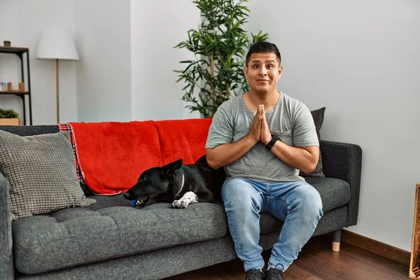 Jovem Latino Homem Cão Sentado Sofá Casa Rezando Com Mãos — Fotografia de Stock