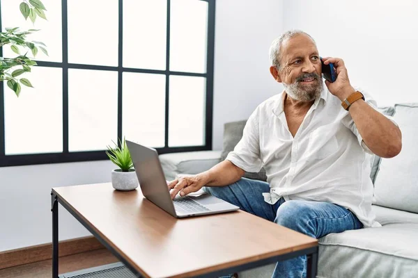 Starší Šedovlasý Muž Mluví Smartphonu Pomocí Notebooku Doma — Stock fotografie